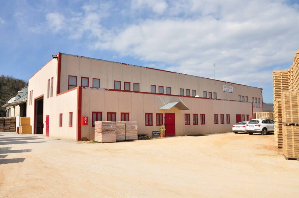 Edificio industriale con auto parcheggiate e pallet accatastati.