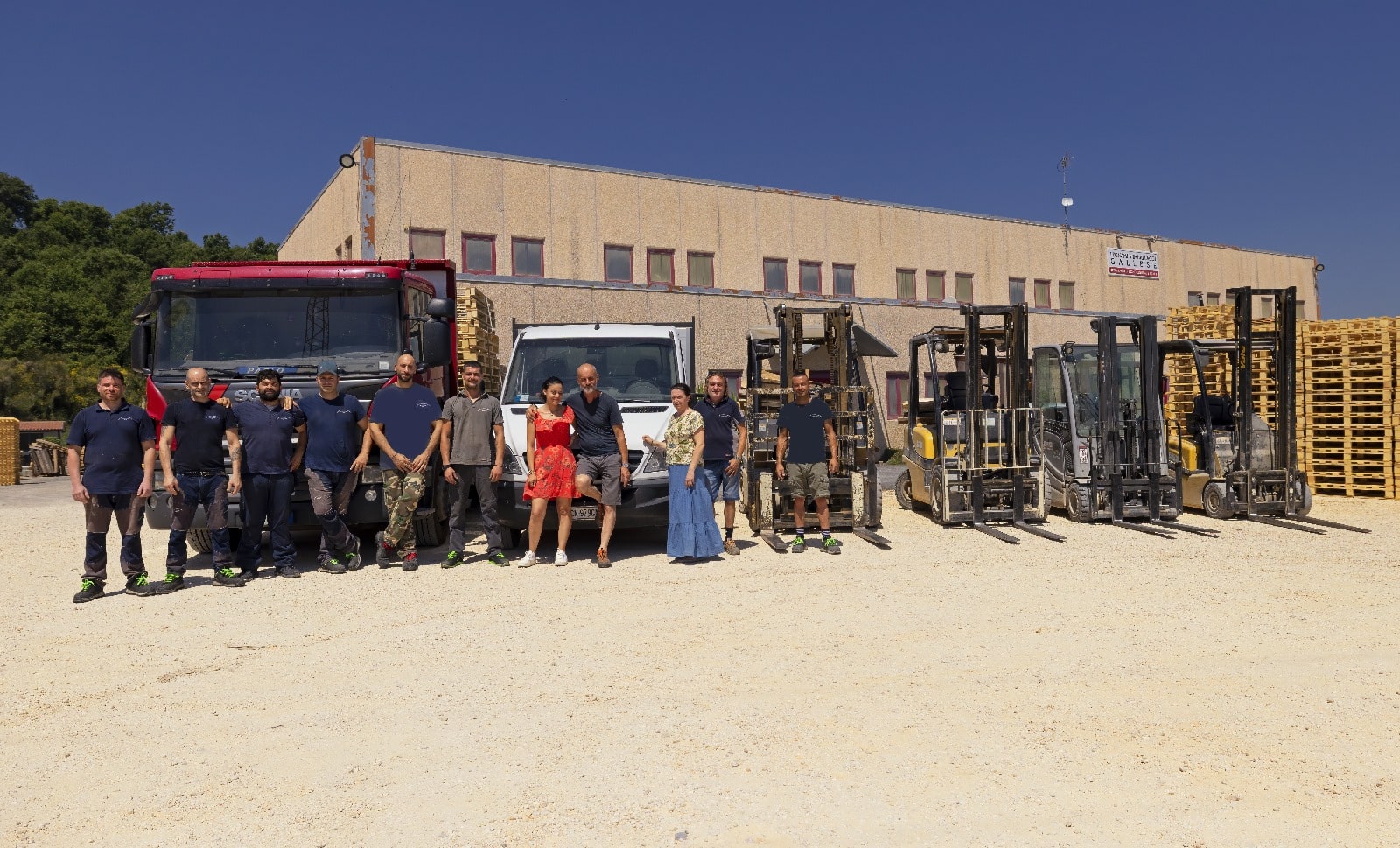 Gruppo di persone davanti a camion e carrelli elevatori.