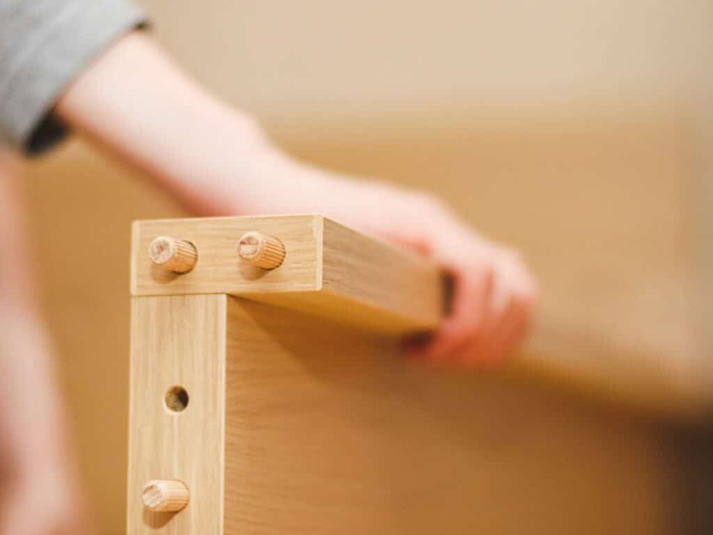 Furniture dowels on a wooden part for a bed with a man's hand